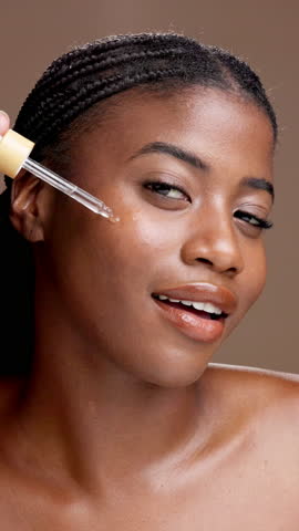 Face, black woman and apply serum for skincare, .salicylic acid or vitamin c. Portrait, cosmetics and happy model with dropper for essential oil, anti aging and hydration on brown studio background