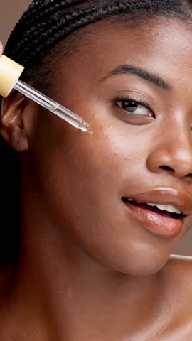 Face, black woman and apply oil for skincare, hyaluronic acid or vitamin c. Portrait, cosmetics and happy model with dropper for serum, anti aging and hydration for health on brown studio background