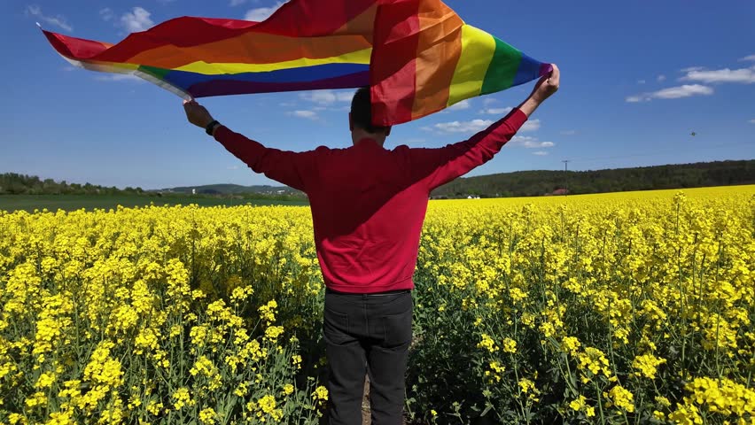 LGBTQ+ visibility: Man with rainbow flag amidst flowering fields	