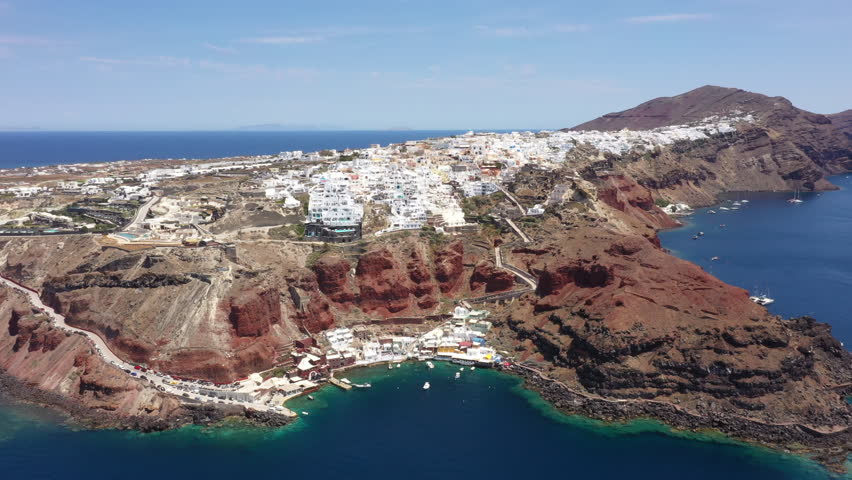 Aerial View of Oia, Santorini With Whitewashed Buildings On Steep Red Cliffs Overlooking Ammoudi Bay In Greece.