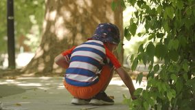 A young boy draws with chalk on a shaded sidewalk, focused and creative. He is surrounded by trees and greenery in a peaceful park in Simferopol, Crimea. - Powered by Shutterstock - Get 15% off with code: PIKWIZARD15