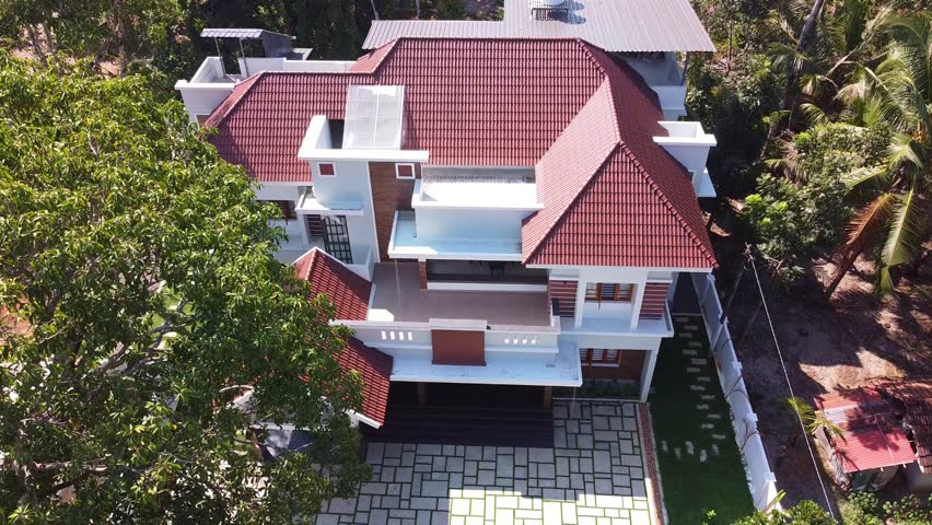Aerial view of a beautiful modern Indian home with sloped tiled roof, spacious balcony, driveway, lush greenery, and elegant architecture. Perfect for showcasing real estate, housing, and urban design