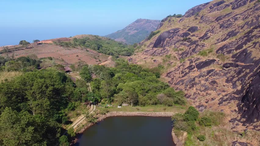 Stunning aerial view of a serene lake nestled in lush green hills and rocky terrain in India. Ideal for nature lovers exploring tranquil landscapes and tourist spots.