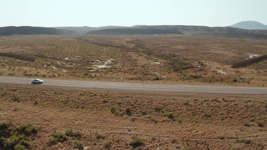 Drone Shot of Desolate road in the Wyoming desert with a white car driving by. This shot tracks left to right
