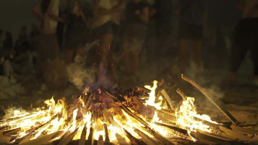 bonfires at st. John night fest in Coruna , Spain , with people unfocused and controlled fire on beach at night , 4k video footage with focus in foreground