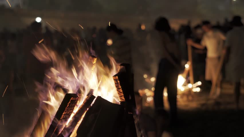 bonfires at st. John night fest in Coruna , Spain , with people unfocused and controlled fire on beach at night , 4k video footage with focus in foreground