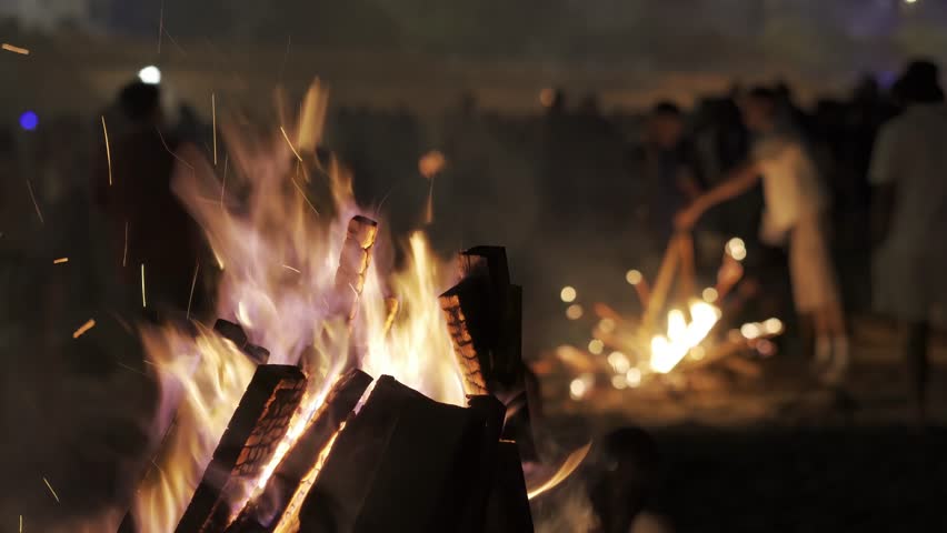 bonfires at st. John night fest in Coruna , Spain , with people unfocused and controlled fire on beach at night , 4k video footage with focus in foreground