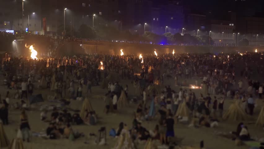 bonfires at st. John night fest in Coruna , Spain , with people unfocused and controlled fire on beach at night , 4k video footage with focus in foreground