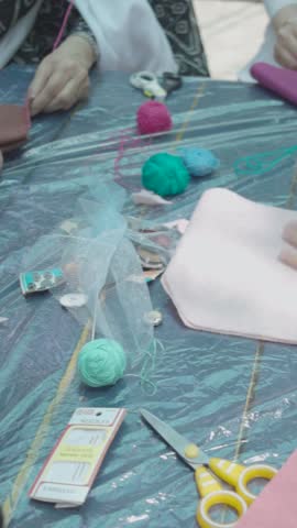 A crafting table filled with yarn balls, scissors, and a partially folded piece of pink felt is shown from above. A child