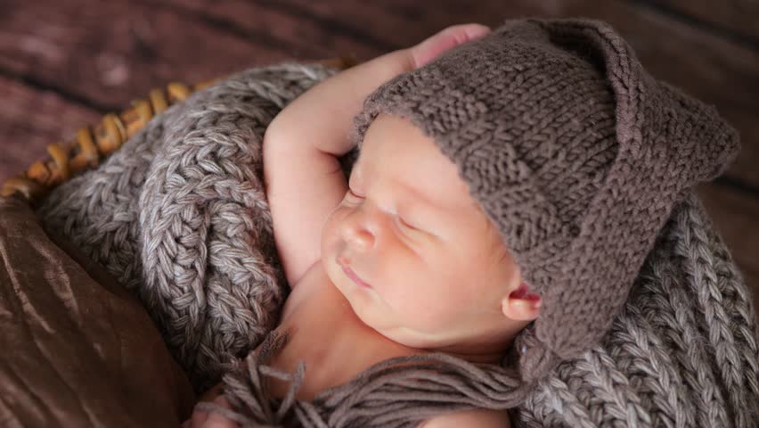Newborn baby sleeps soundly adorned with knitted hat and wrapped in textured blanket. Infant boy nestled in basket creating warm scene