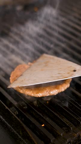 A raw beef burger patty sits directly on a clean metal grill grate, just beginning to cook. Wisps of smoke rise from the grates, while the light brown patty remains unseasoned and untouched