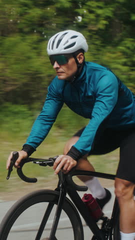 Cyclist in protective hard hat rides bicycle across green forest. Male rider speeding on fast vehicle trains for sports competition at calm countryside