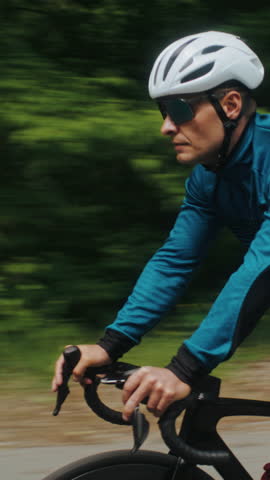 Cyclist in protective hard hat rides bicycle across green forest. Male rider speeding on fast vehicle trains for sports competition at calm countryside