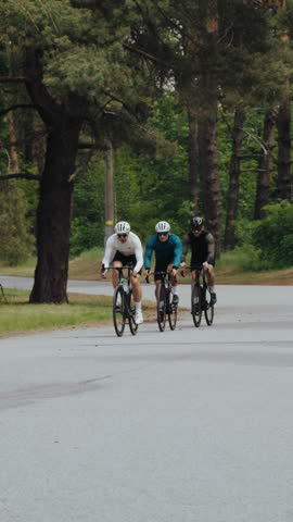 Young sportsmen in tracksuits ride bicycles along winding road. Professional athletic team on fast bikes prepares for racing at summer countryside