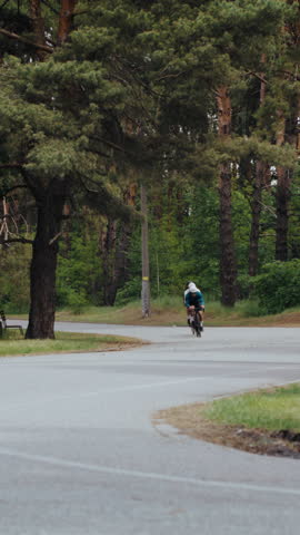 Determined sportsmen ride bicycles fast along winding road in forest. Professional athletic men on bikes depict spirit of rivalry during racing at countryside