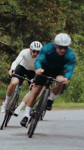 Determined sportsmen ride bicycles fast along winding road in forest. Professional athletic men on bikes depict spirit of rivalry during racing at countryside