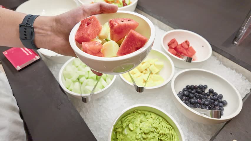 Closeup of man holding bowl adding fresh fruit from breakfast fruit buffet, , healthy hotel breakfast choices