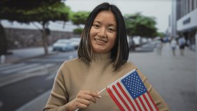 Young chinese woman holding american flag smiling on a city street, symbolizing cultural diversity and international connection in an urban outdoor setting. - Powered by Shutterstock - Get 15% off with code: PIKWIZARD15