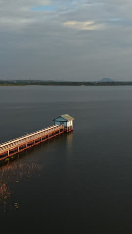 Rotating lakeside pumping station view, revealing tranquil water surface, wooden pier, misty hillside landscape
