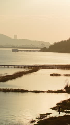 Tranquil lake view with wooden pier and distant hills at sunset in bang phra, thailand