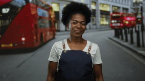 Woman smiling outdoors in city wearing apron with double-decker bus in background, capturing urban lifestyle, diverse culture, and casual fashion in streetscape. - Powered by Shutterstock - Get 15% off with code: PIKWIZARD15