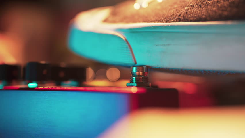 A guitarist engages an effect pedal footswitch with their foot.