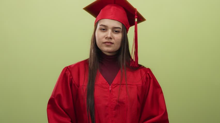 Woman in red graduation gown gestures no against yellow background, expressing confidence and determination, a symbol of achievement and future aspirations.