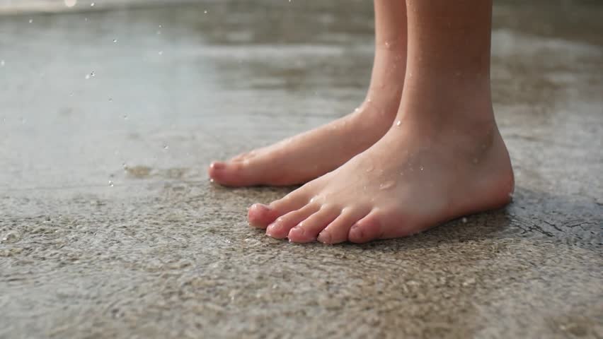 Close-up of a child's bare feet stomping in a rain puddle on paving slabs