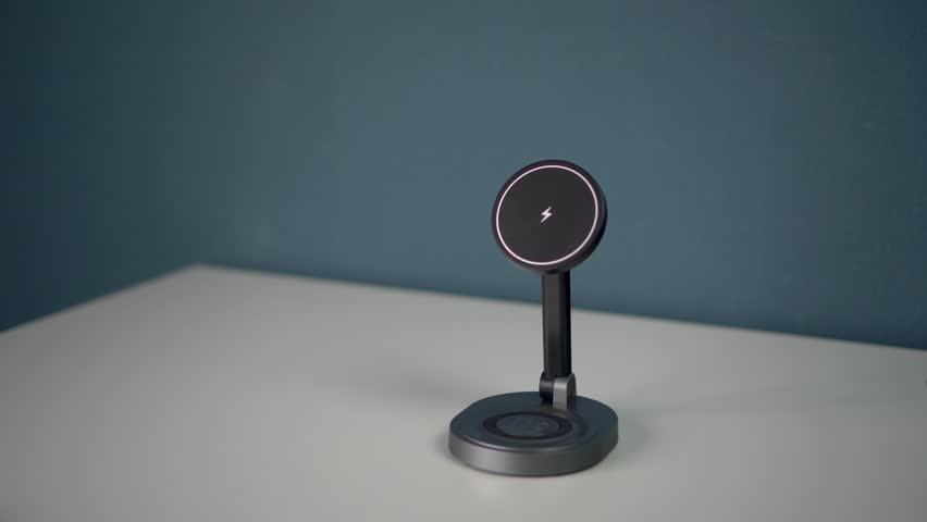 A phone with a black screen is placed on a magnetic stand with wireless charging, located on a free and minimalist table.