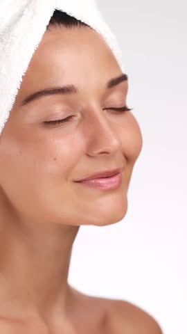 Young Caucasian woman smiles softly and touches her cheek after a skincare routine. Perfect for cosmetic ads, wellness branding, self-care lifestyle content, and beauty product visuals.