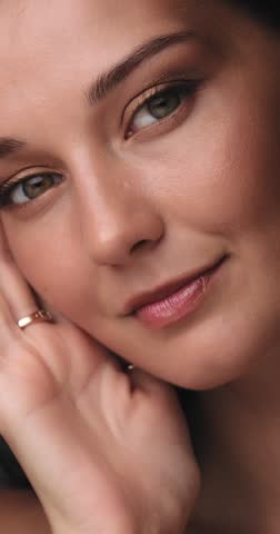 Caucasian woman with glowing skin and shimmering gold eye shadow poses with her hands near face, highlighting elegant jewelry and makeup in a high-end commercial beauty concept.