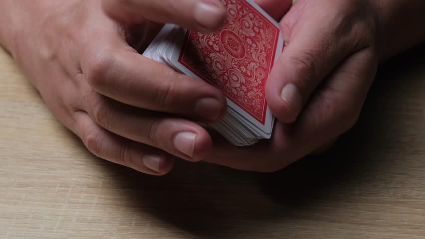 Close-up of Hands Shuffling Red Playing Cards on Wooden Surface for Card Games and Magic Tricks