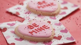 Slow Motion: Red and White Sprinkles Falling on Pink Frosted "Be Mine" Heart Cookies. Sweet Valentine's Day Dessert. - Powered by Shutterstock - Get 15% off with code: PIKWIZARD15