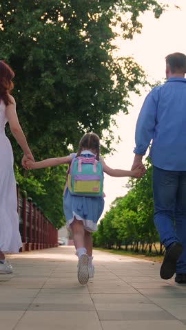 Girl with parents running to school. Children education concept. Child daughter with backpacks, father mother running to school holding hands. Happy family. Mom dad taking child to school along street