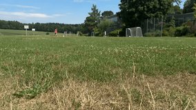 Football field with kids playing in the background, sunny summer day in suburban area, green grass, sports training outdoors, youth soccer practice in distance - Powered by Shutterstock - Get 15% off with code: PIKWIZARD15