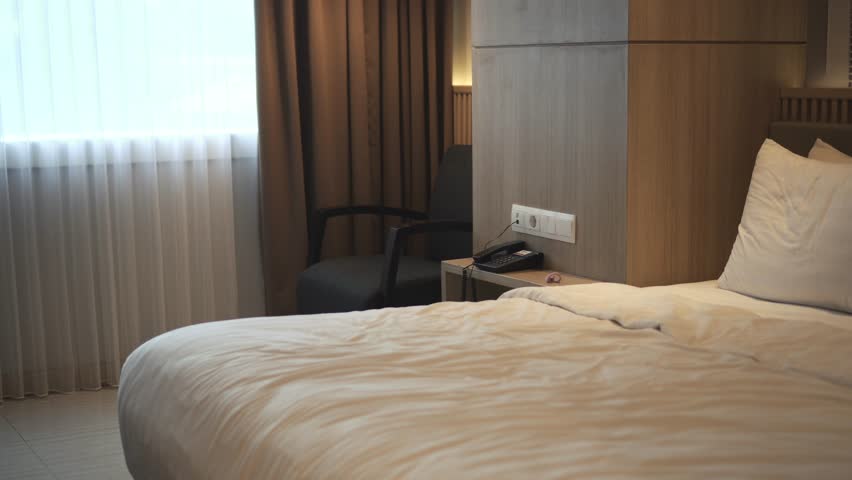 A Muslim woman wearing a hijab relaxes and lies on the bed after arriving at a hotel room.