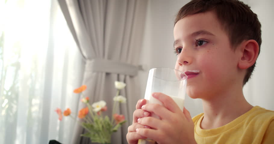 Cute Handsome child drinking milk.Healthy eating a child eating breakfast kid dream concept. Funny little boy in kitchen drinks yogurt milk and licks her lips.Positive kid smiling having breakfast. 4K