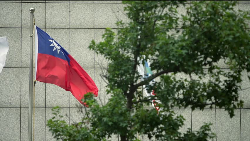 Slow motion of Taiwan flag as seen through tree branches, with a modern building in the background. The scene captures national pride and the integration of nature and city life.