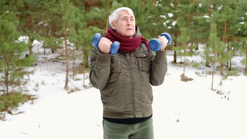 Senior man working out outdoors in winter forest. Person lifting dumbbells. Old male exercising. Healthy people lifestyle. Active sport training. Older elderly sportsman doing fitness. Workout session