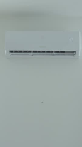 Close-up of hand using remote control to adjust temperature on wall-mounted air conditioner. Concept of indoor climate control and cooling during hot weather