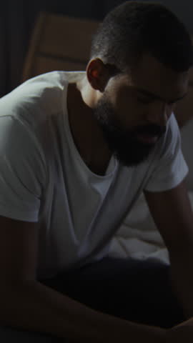 Black guy expresses suffering and brokenness sitting on messy bed. African American male stays alone in world feeling fatigues of depression at home