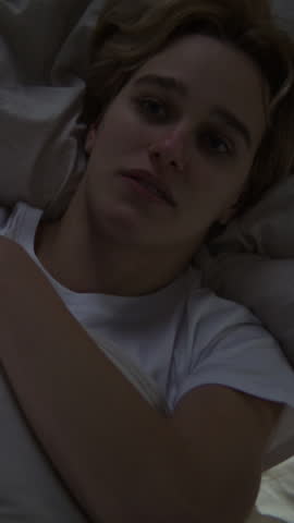 Upset young woman hugs pillow lying in bed at night. Blonde female with dark circles under eyes due to crying tries to deal with negative emotions