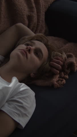 Young woman lies on couch appearing lost in thought. Female performs contemplative state suggesting deep introspection or period of confusion in life