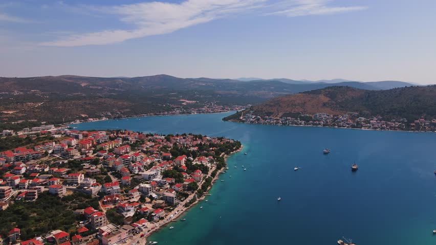 Scenic waterfront town on Adriatic Sea with calm blue water, boats and surrounding mountains in bay. Panoramic aerial view of Mediterranean shoreline