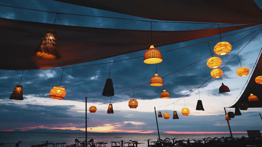 Glowing lanterns create a magical ambiance against a vibrant sunset over the sea in this slow motion video