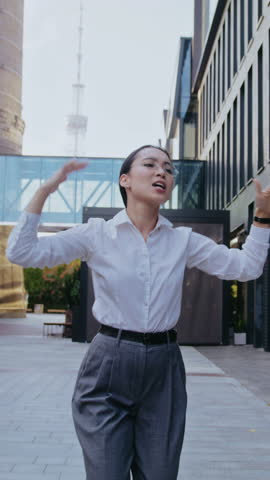 Asian businesswoman celebrates success dancing and singing in business district. Young woman radiates joy and excitement filling atmosphere with career achievement happiness