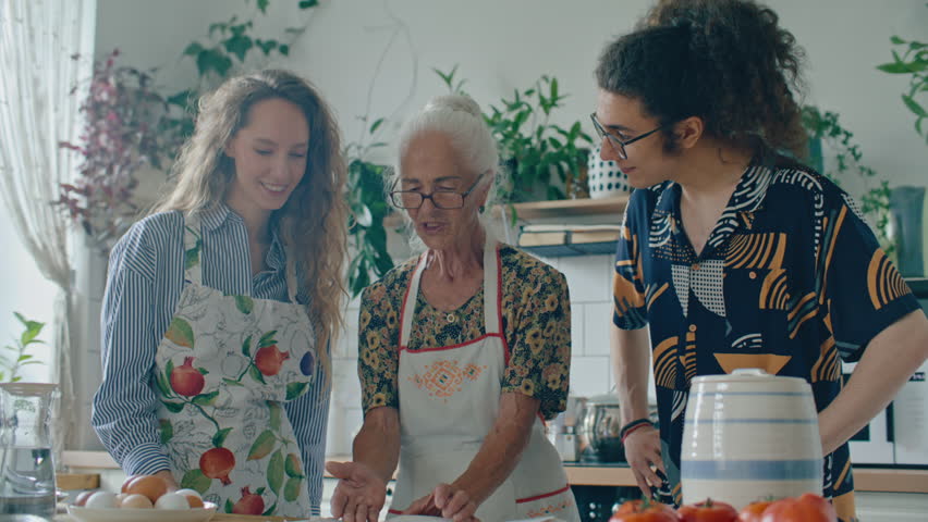 Elderly grandmother in apron explaining handwritten family recipe from book to young grandson and granddaughter before cooking meal together in home kitchen