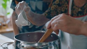 Hands of senior woman pouring olive oil into steaming pot as granddaughter stirring sauce with wooden spoon during home meal preparation in kitchen. Close-up view - Powered by Shutterstock - Get 15% off with code: PIKWIZARD15