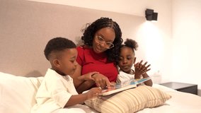 Loving african american mother nurturing children's imagination, reading bedtime story while sitting comfortably in bedroom, sharing peaceful family moment together - Powered by Shutterstock - Get 15% off with code: PIKWIZARD15