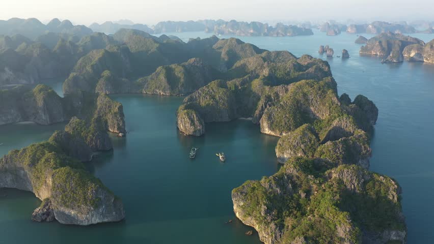 Vietnamese traditional junks sailing gracefully across limestone karsts of UNESCO World Heritage Site Ha Long Bay, showcasing natural beauty and cultural maritime heritage